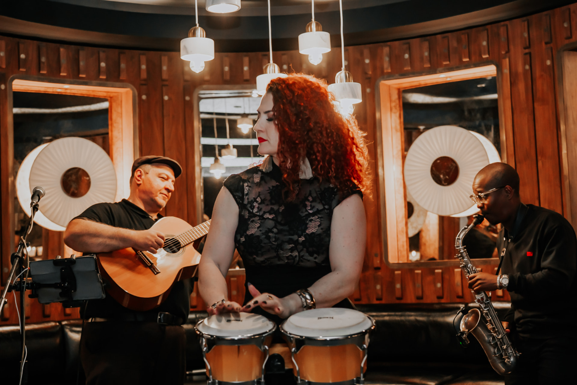 René Hunter playing bongos, eyes closed, flanked by guitarist and saxophonist.