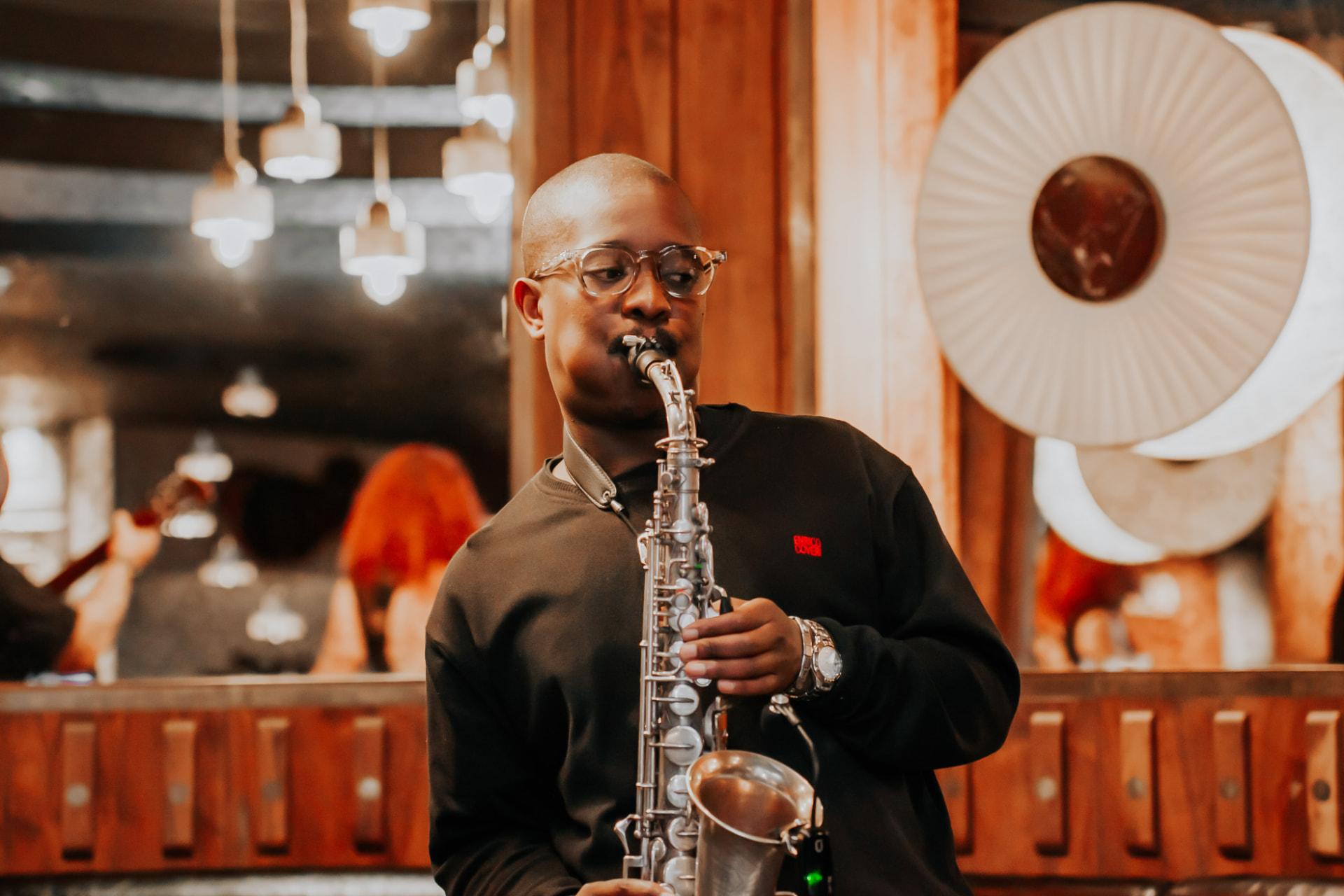 Saxophonist playing an alto saxophone under pendant lighting.